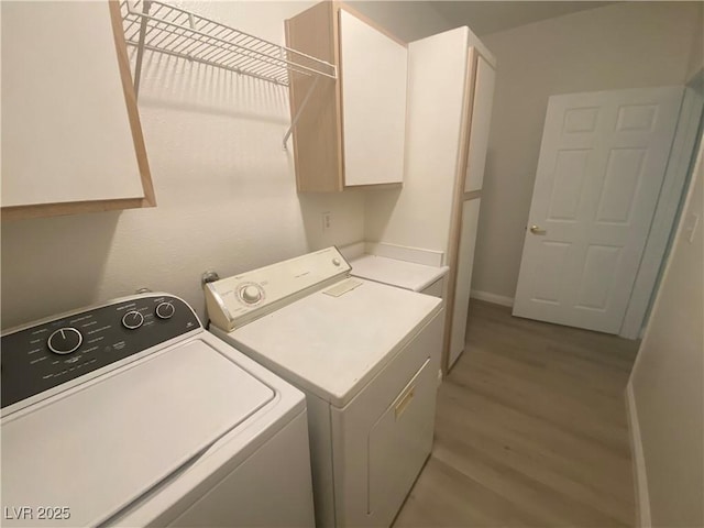 clothes washing area with cabinets, light wood-type flooring, and separate washer and dryer