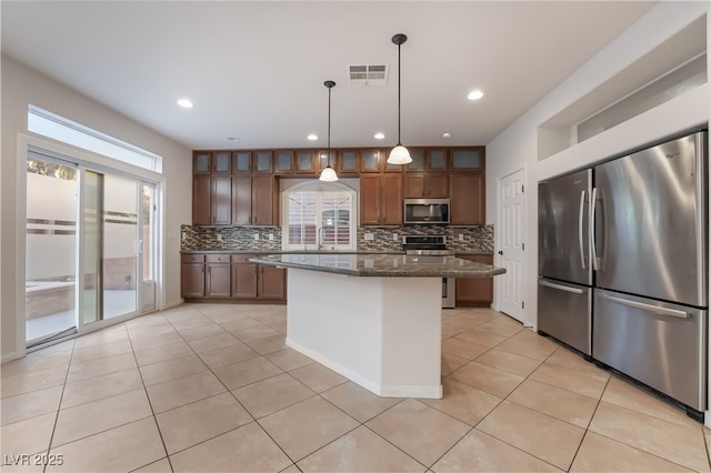 kitchen with appliances with stainless steel finishes, a center island, dark stone counters, and a healthy amount of sunlight