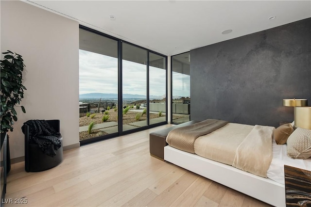 bedroom featuring a mountain view, access to outside, floor to ceiling windows, and light hardwood / wood-style floors