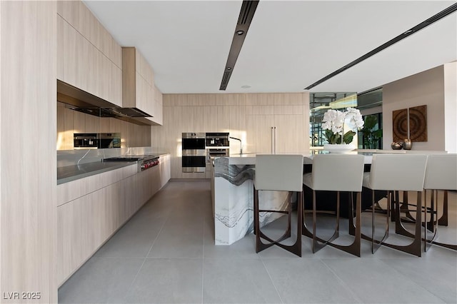 kitchen with a kitchen bar, light brown cabinetry, light tile patterned floors, and appliances with stainless steel finishes