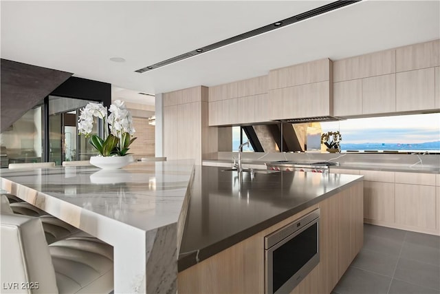 kitchen with light brown cabinetry, sink, dark tile patterned flooring, a center island, and stainless steel microwave