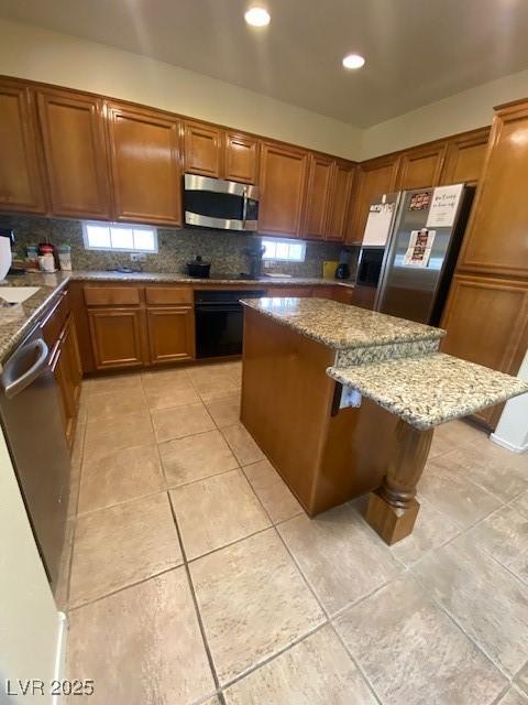 kitchen featuring a center island, decorative backsplash, light stone counters, appliances with stainless steel finishes, and a kitchen bar