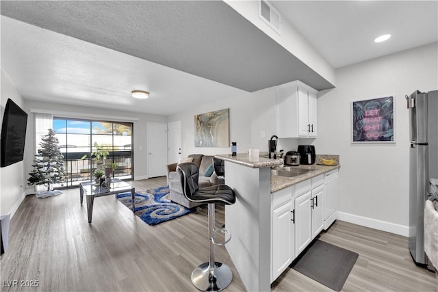 kitchen featuring white cabinets, a kitchen breakfast bar, sink, light stone countertops, and kitchen peninsula