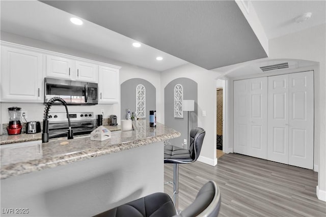 kitchen featuring a kitchen bar, appliances with stainless steel finishes, light stone counters, light hardwood / wood-style flooring, and white cabinetry