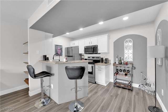 kitchen featuring white cabinets, a kitchen bar, light wood-type flooring, and stainless steel appliances