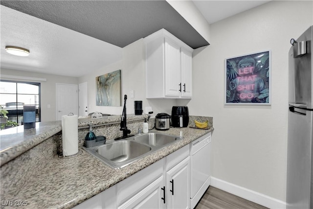 kitchen with white dishwasher, sink, hardwood / wood-style flooring, white cabinetry, and stainless steel refrigerator