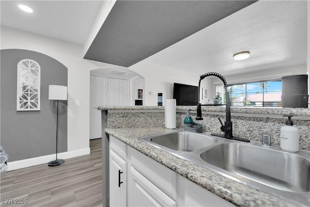 kitchen with light stone countertops, a textured ceiling, sink, light hardwood / wood-style flooring, and white cabinetry