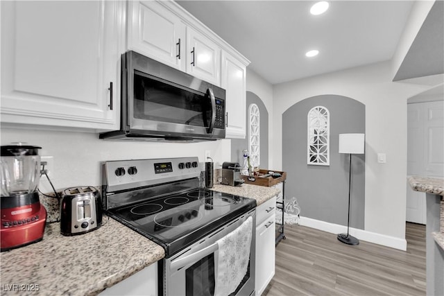 kitchen featuring white cabinets, light hardwood / wood-style floors, light stone counters, and appliances with stainless steel finishes