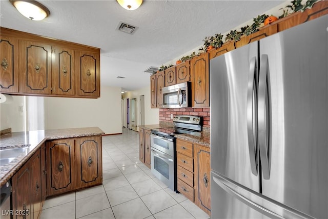 kitchen featuring kitchen peninsula, a textured ceiling, decorative backsplash, light tile patterned floors, and appliances with stainless steel finishes