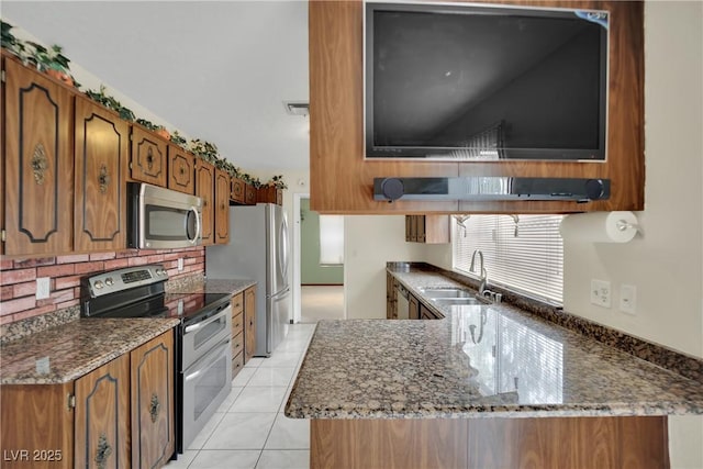 kitchen featuring kitchen peninsula, appliances with stainless steel finishes, sink, light tile patterned floors, and dark stone countertops