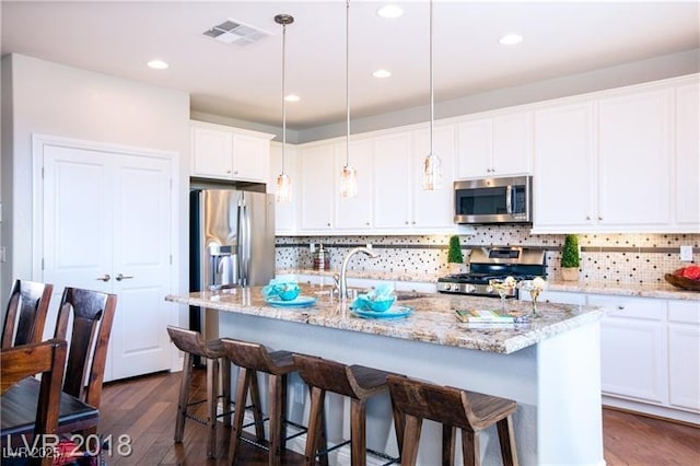 kitchen with appliances with stainless steel finishes, decorative light fixtures, white cabinets, dark hardwood / wood-style flooring, and a kitchen island with sink