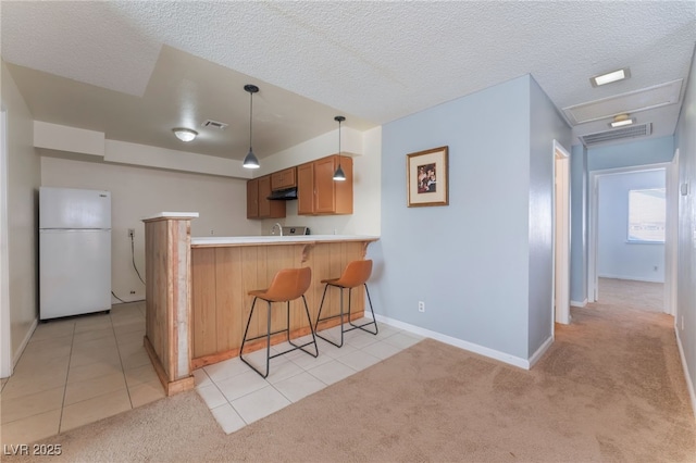 kitchen featuring pendant lighting, white fridge, a kitchen breakfast bar, kitchen peninsula, and light tile patterned floors