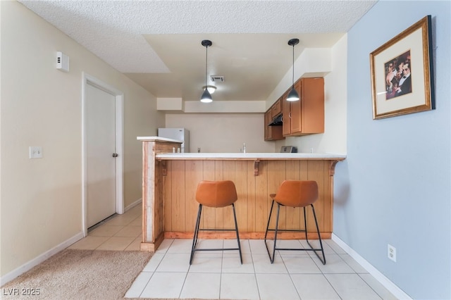 kitchen with decorative light fixtures, kitchen peninsula, a kitchen breakfast bar, light tile patterned floors, and white refrigerator