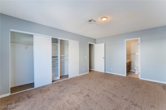 unfurnished bedroom featuring light colored carpet, multiple closets, connected bathroom, and a textured ceiling