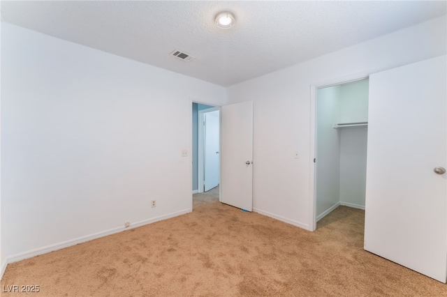 unfurnished bedroom featuring light colored carpet, a textured ceiling, a closet, and a walk in closet