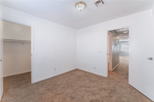 unfurnished bedroom with a textured ceiling, a closet, a walk in closet, and carpet