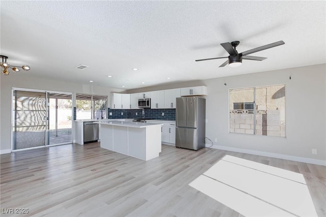 kitchen with appliances with stainless steel finishes, ceiling fan, a kitchen island, white cabinets, and light hardwood / wood-style flooring