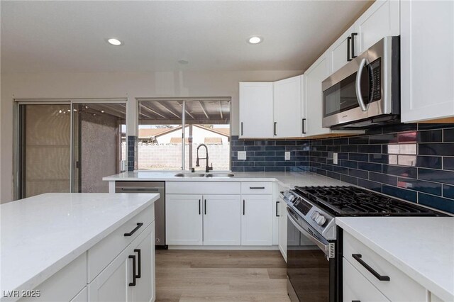 kitchen with light hardwood / wood-style flooring, stainless steel appliances, backsplash, white cabinets, and sink