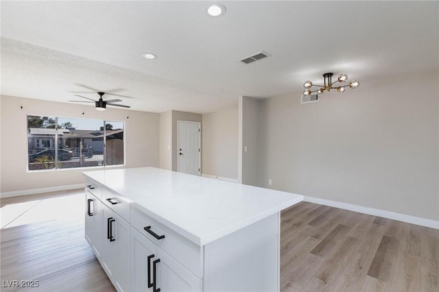 kitchen with a textured ceiling, a center island, light wood-type flooring, ceiling fan with notable chandelier, and white cabinets