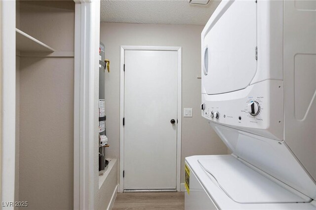 clothes washing area featuring a textured ceiling, light hardwood / wood-style floors, and stacked washer / drying machine