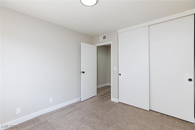 unfurnished bedroom with a textured ceiling, light colored carpet, and a closet