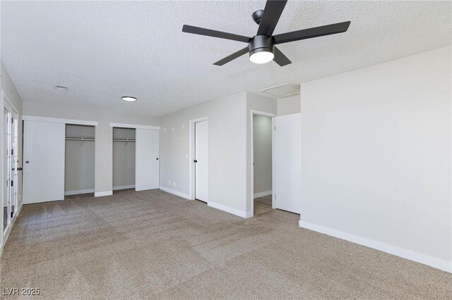 unfurnished bedroom with light carpet, a textured ceiling, ceiling fan, and two closets