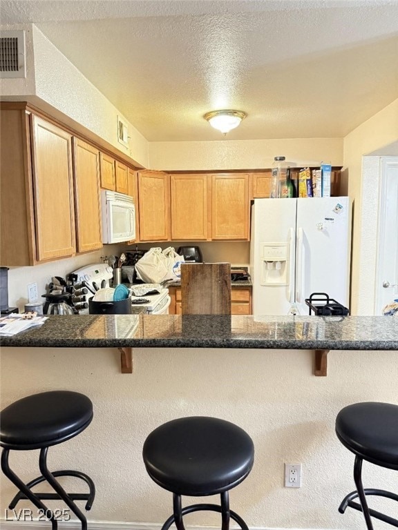 kitchen featuring a breakfast bar area, kitchen peninsula, a textured ceiling, and white appliances