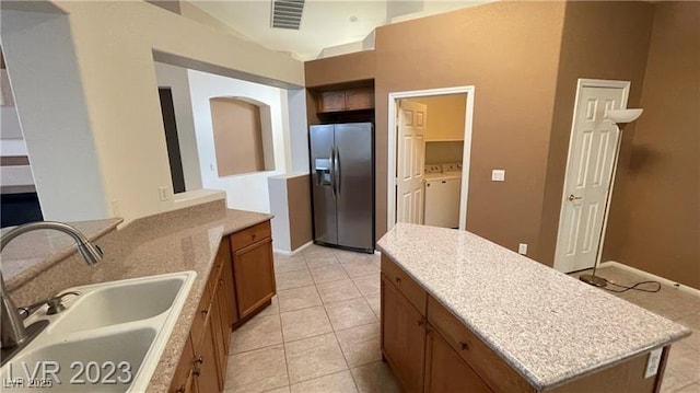 kitchen featuring light tile patterned floors, stainless steel refrigerator with ice dispenser, a kitchen island, washing machine and clothes dryer, and sink