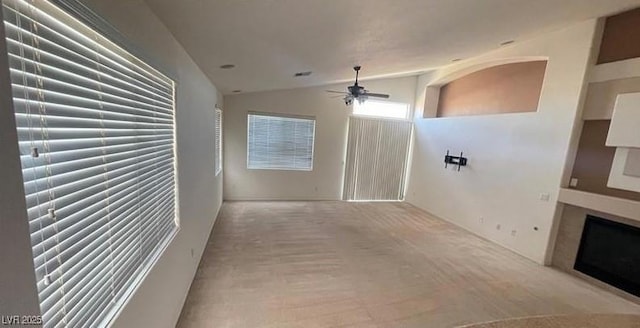 unfurnished living room featuring lofted ceiling, ceiling fan, and light colored carpet