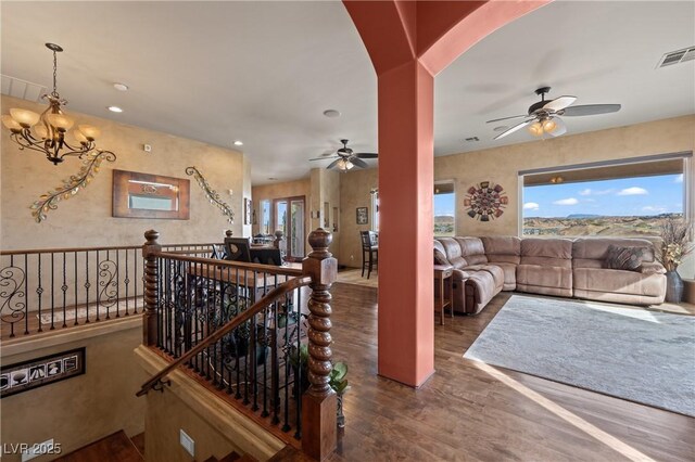 living room with ceiling fan with notable chandelier and dark hardwood / wood-style flooring