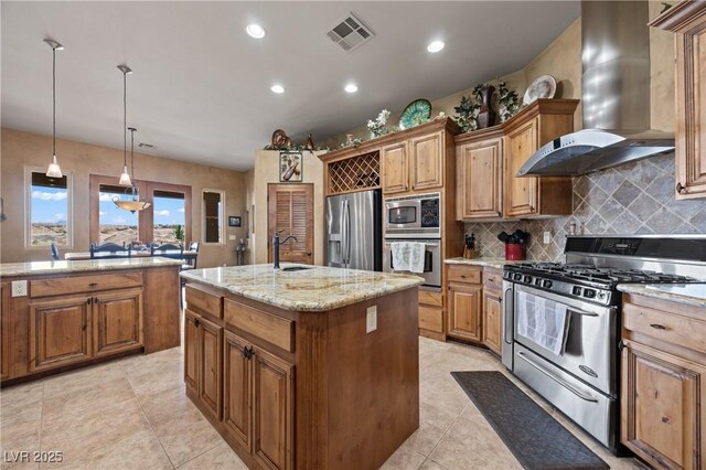 kitchen with appliances with stainless steel finishes, light stone counters, wall chimney exhaust hood, a center island with sink, and decorative light fixtures