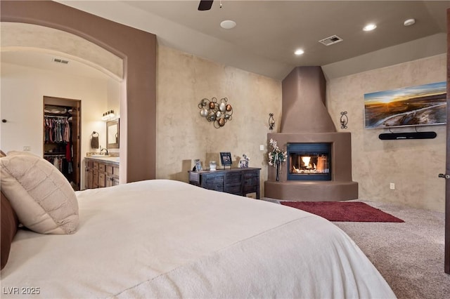 bedroom featuring lofted ceiling, carpet flooring, sink, a large fireplace, and a walk in closet