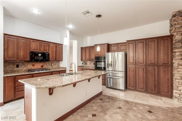 kitchen featuring decorative light fixtures, a center island with sink, black appliances, sink, and a breakfast bar area