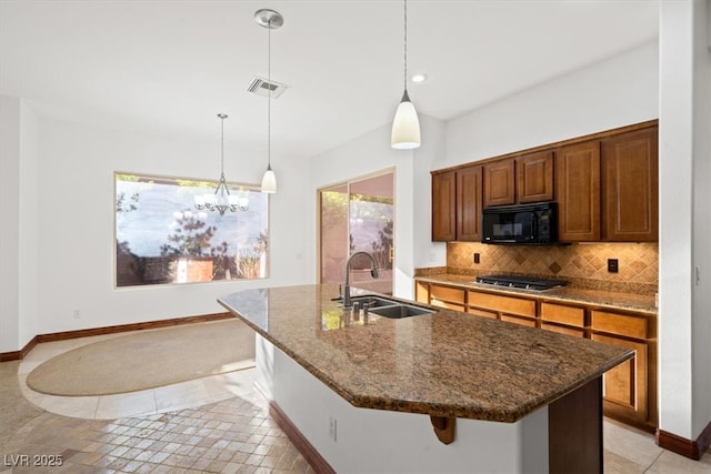 kitchen featuring tasteful backsplash, visible vents, stainless steel gas stovetop, black microwave, and a sink