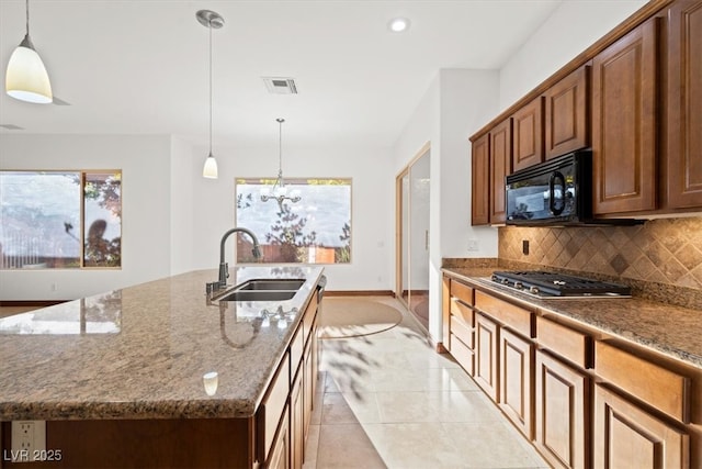 kitchen featuring stone countertops, decorative backsplash, stainless steel gas stovetop, black microwave, and a sink