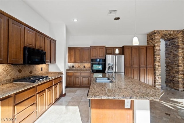 kitchen with a sink, visible vents, black appliances, tasteful backsplash, and a center island with sink