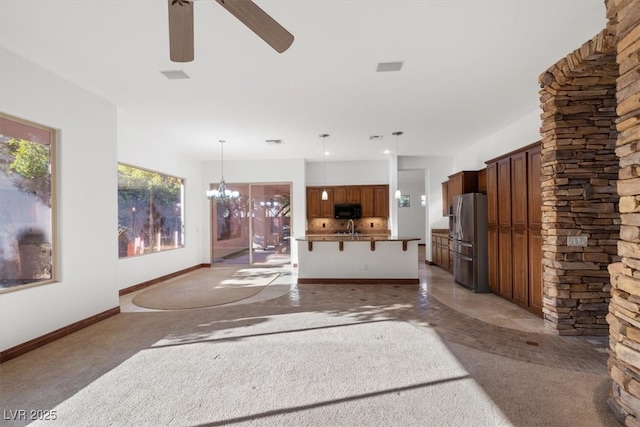 unfurnished living room with a sink, baseboards, a wealth of natural light, and ceiling fan with notable chandelier