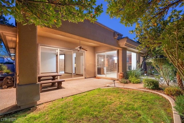 back of property with a lawn, ceiling fan, a patio, and stucco siding