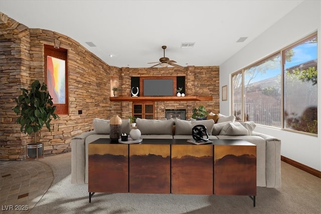 interior space featuring baseboards, visible vents, a ceiling fan, and a stone fireplace