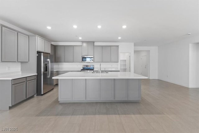 kitchen with gray cabinetry, a center island with sink, stainless steel appliances, and sink