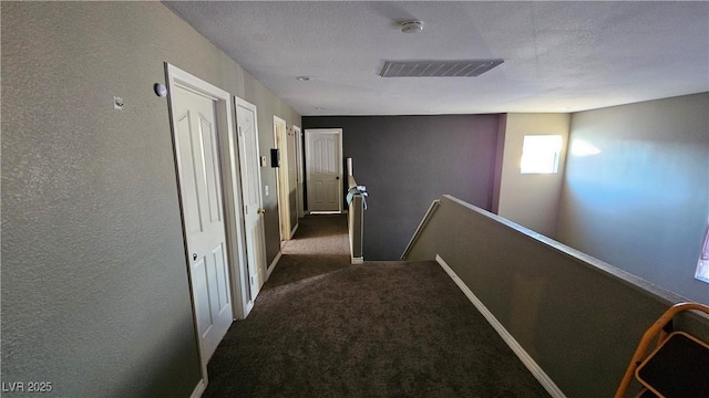 hall with a textured ceiling and dark carpet