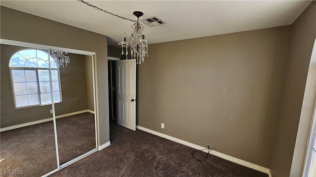 unfurnished bedroom featuring a chandelier, dark carpet, and a closet