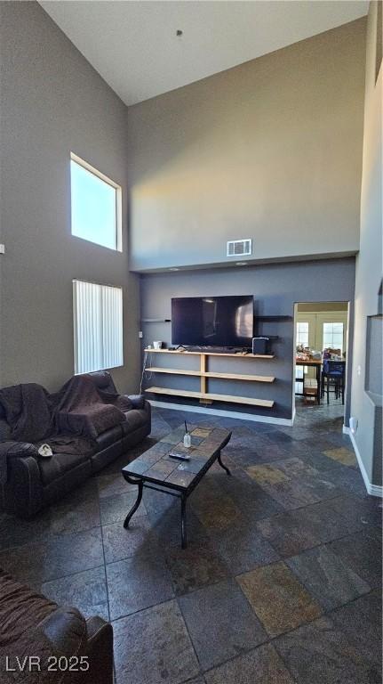 living area featuring a towering ceiling, baseboards, and visible vents