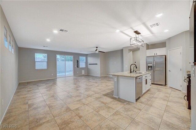 kitchen with white cabinetry, ceiling fan, hanging light fixtures, stainless steel appliances, and an island with sink