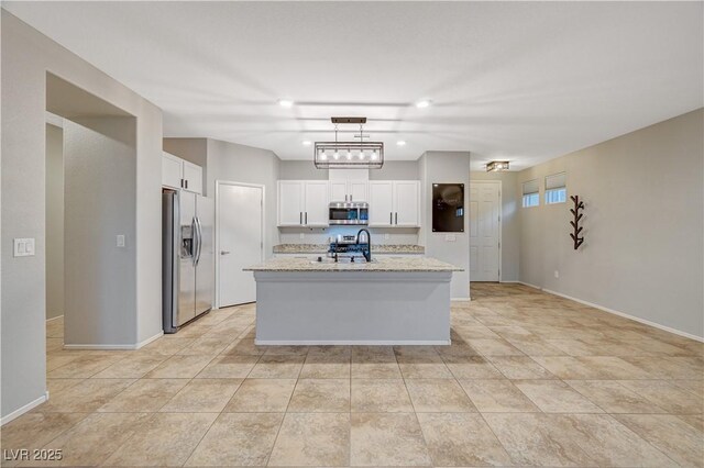 kitchen featuring white cabinets, an island with sink, appliances with stainless steel finishes, decorative light fixtures, and light stone counters