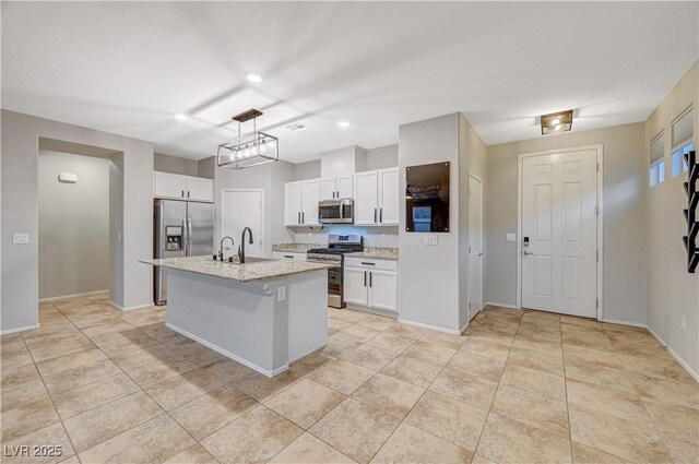 kitchen featuring light stone countertops, appliances with stainless steel finishes, a kitchen island with sink, white cabinetry, and hanging light fixtures