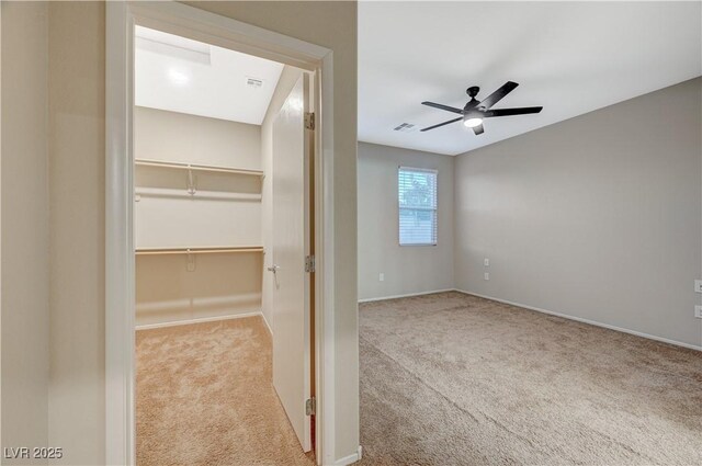 unfurnished bedroom with ceiling fan, a walk in closet, light carpet, and a closet