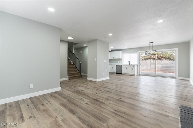 unfurnished living room with a textured ceiling, sink, and light hardwood / wood-style flooring