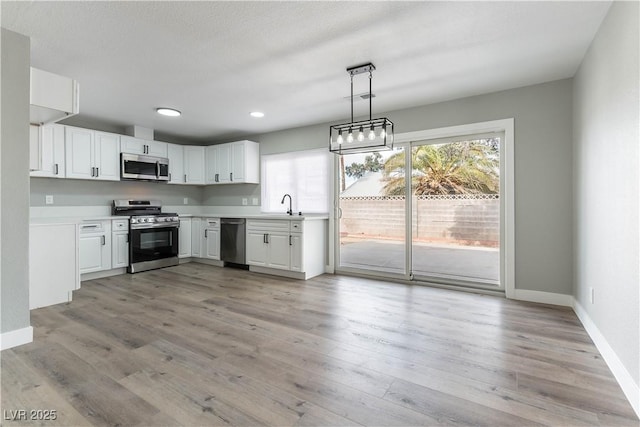 kitchen featuring decorative light fixtures, light wood-type flooring, white cabinetry, and appliances with stainless steel finishes