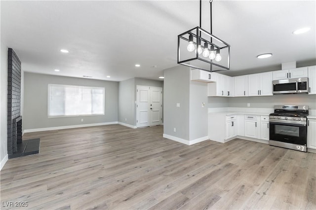 kitchen with a brick fireplace, stainless steel appliances, decorative light fixtures, light hardwood / wood-style flooring, and white cabinets